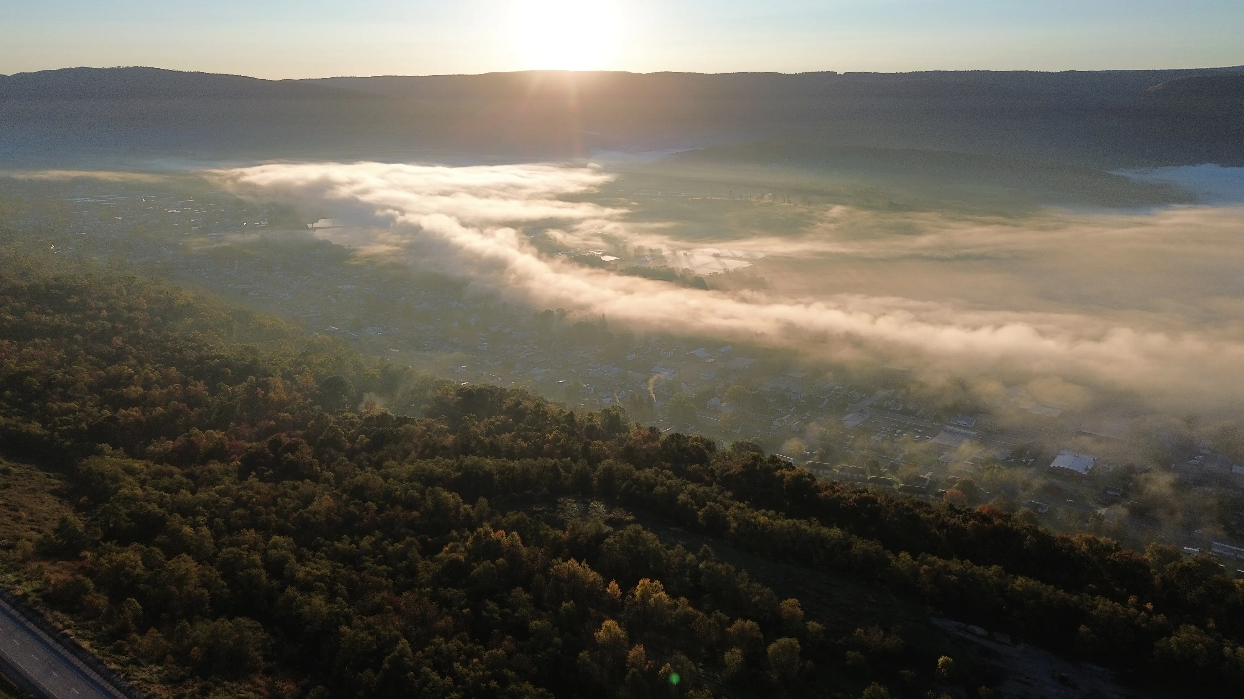 Morning fog lifting through dark wooded hills at sunrise.