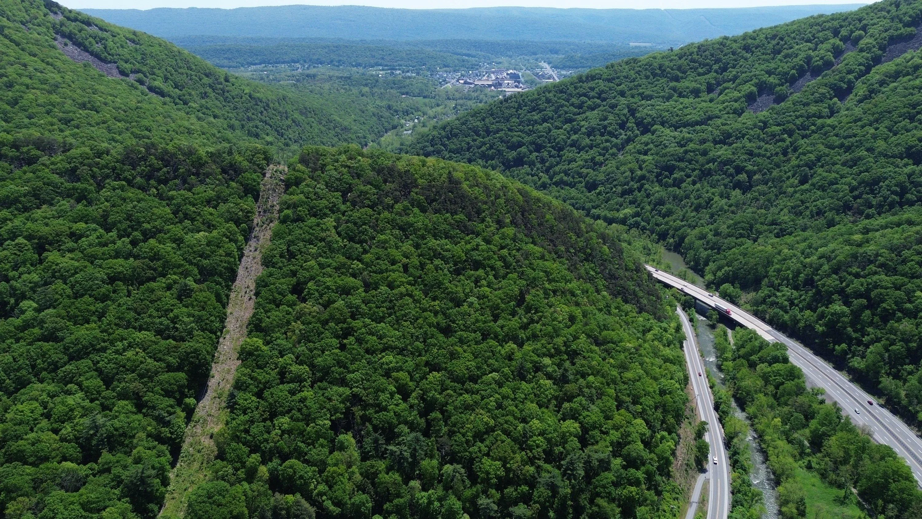 Aerial view down a green mountain gap with a road and river cutting through the valley.