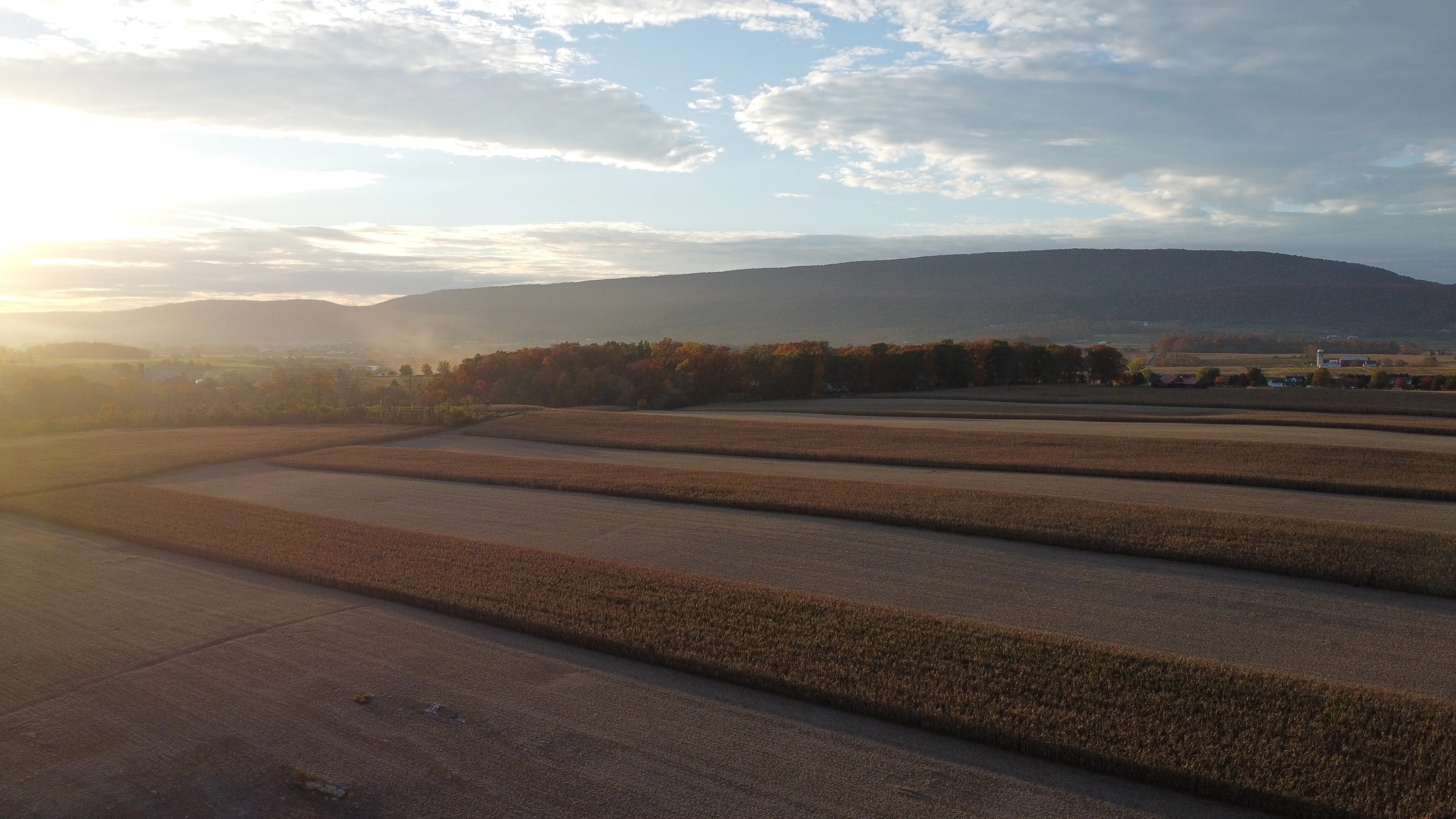 Low sun over brown farm fields with a blue mountain ridge in the distance.