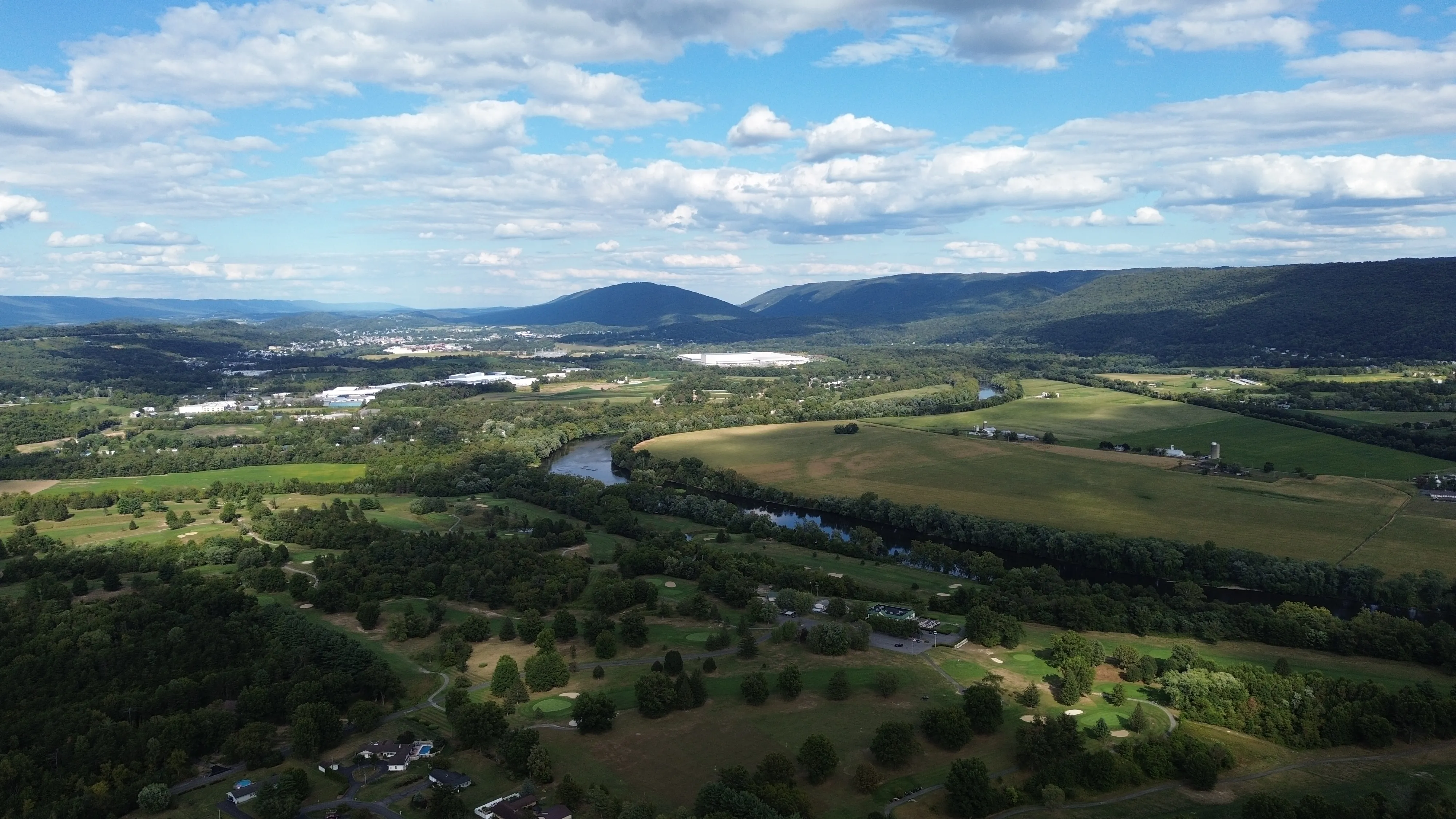 Wide valley landscape with rolling green hills, a winding river, and scattered farm buildings.